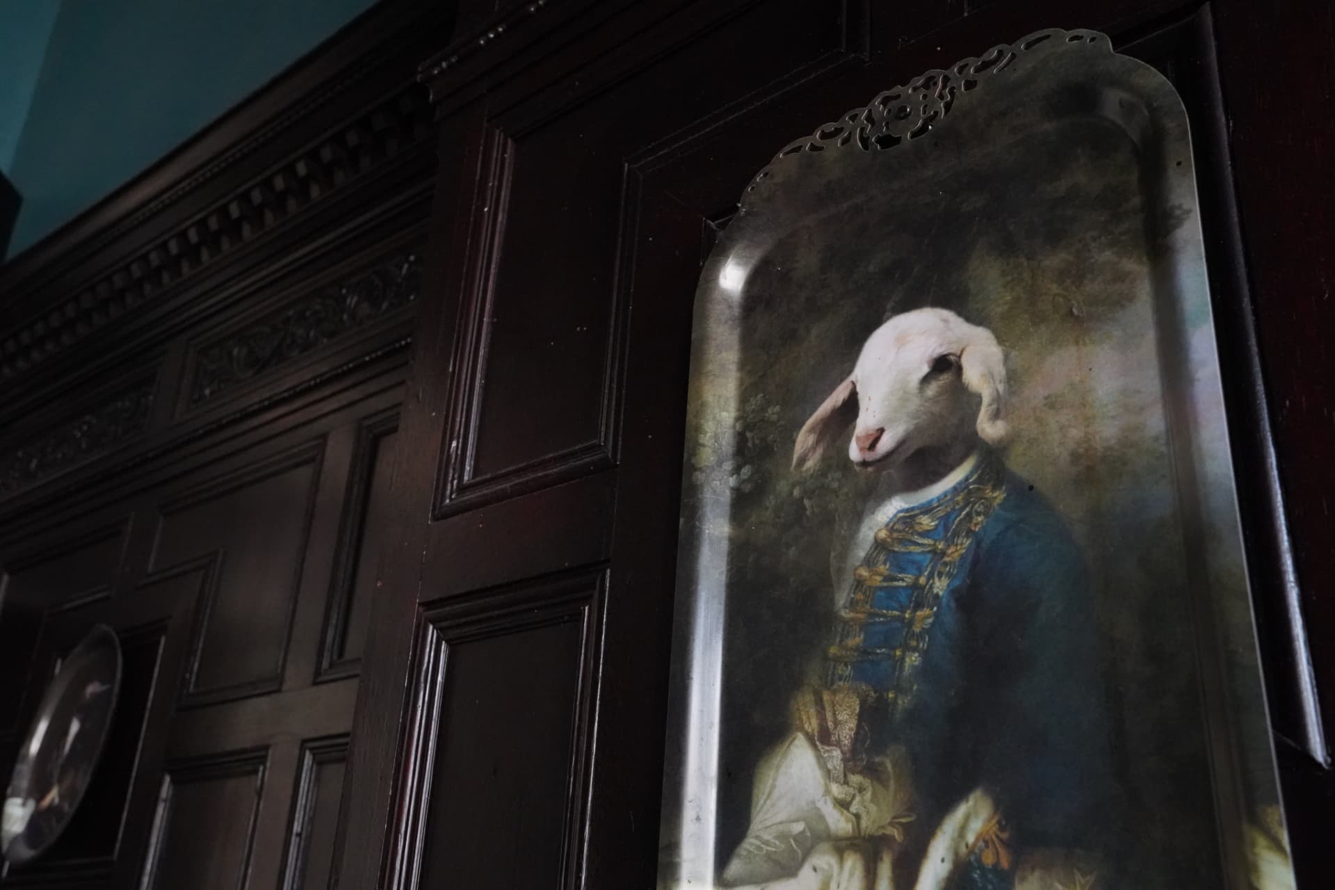 An antique portrait of a lamb in an 18th-century blue coat, hung on dark panelling inside The Milk Thistle