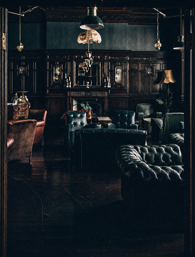 The Parlour at The Milk Thistle, a dark wood panelled Victorian drawing room lit by antique lamps