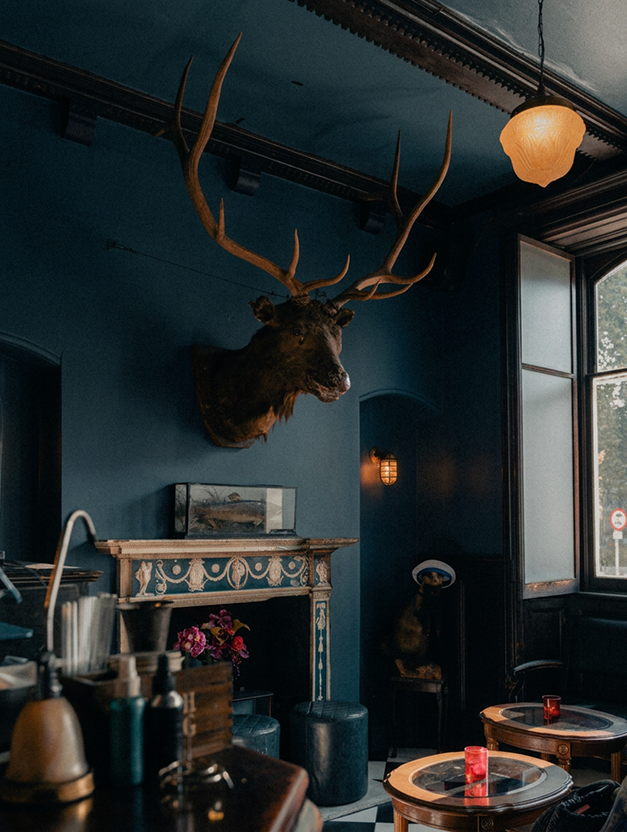 The Lounge at The Milk Thistle with a stag's head above a fireplace and deep teal panelled walls